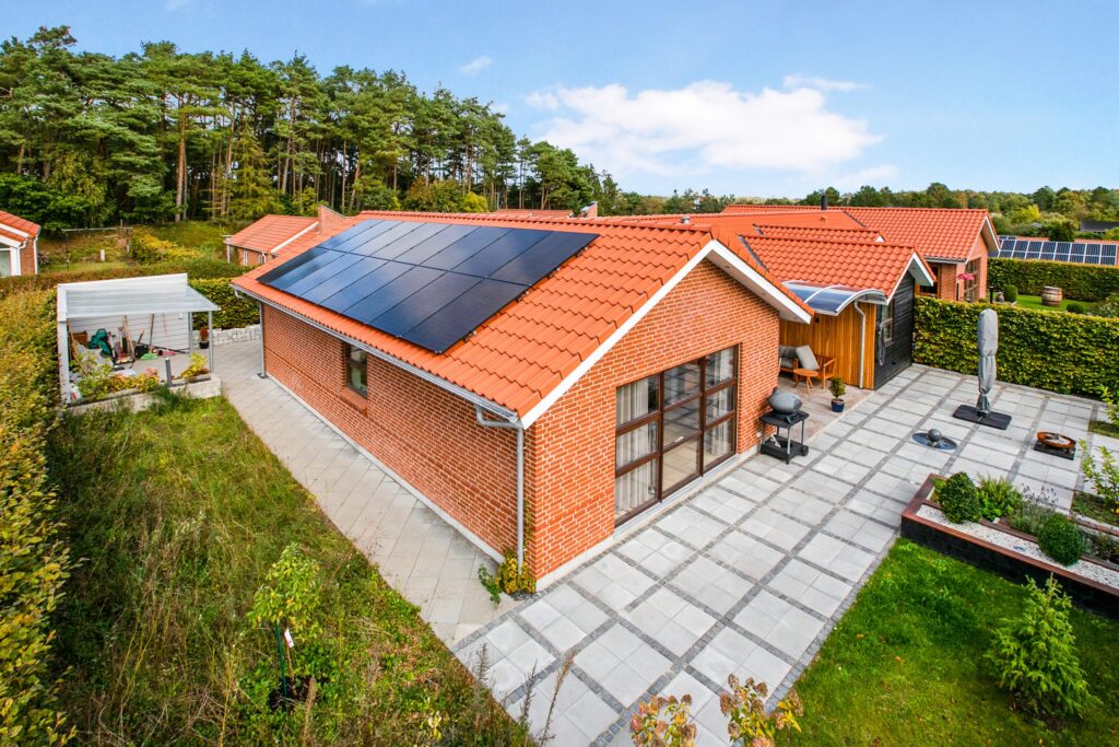 Et nyrenoveret tag med sorte solcellepaneler på et rødstenshus med terrasser og beplantning.