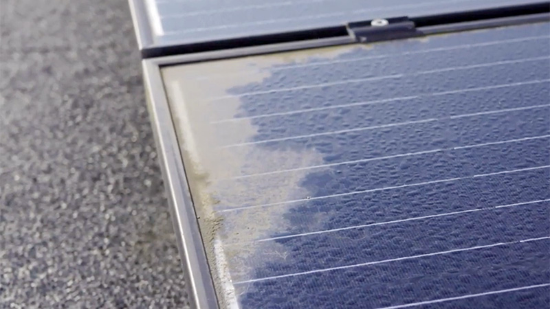 Tæt på et rammeløs solcellepanel med vanddråber og snavs.