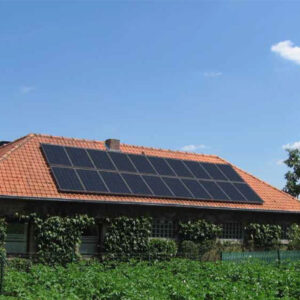 Rødt tegltag med solcellepaneler på et gammelt hus omgivet af grønne planter under blå himmel.